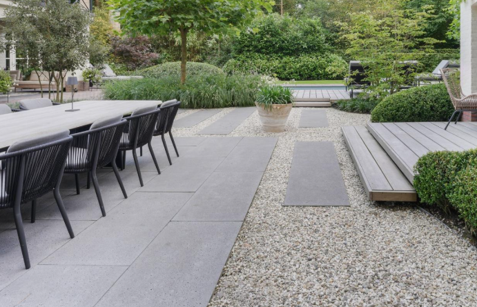 Kiemo apželdinimo pavyzdys su moderniomis dangomis – elegantiškas kiemo dizainas su didelio formato betoninėmis plokštėmis, dekoratyviniu žvyru ir medinėmis terasomis
